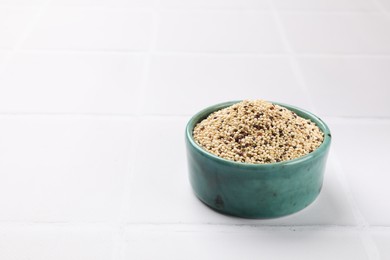 Photo of Raw quinoa seeds in bowl on white table, closeup. Space for text