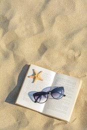 Photo of Beautiful sunglasses, book and starfish on sand, top view. Space for text