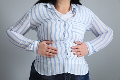 Photo of Overweight woman in tight shirt on light grey background, closeup
