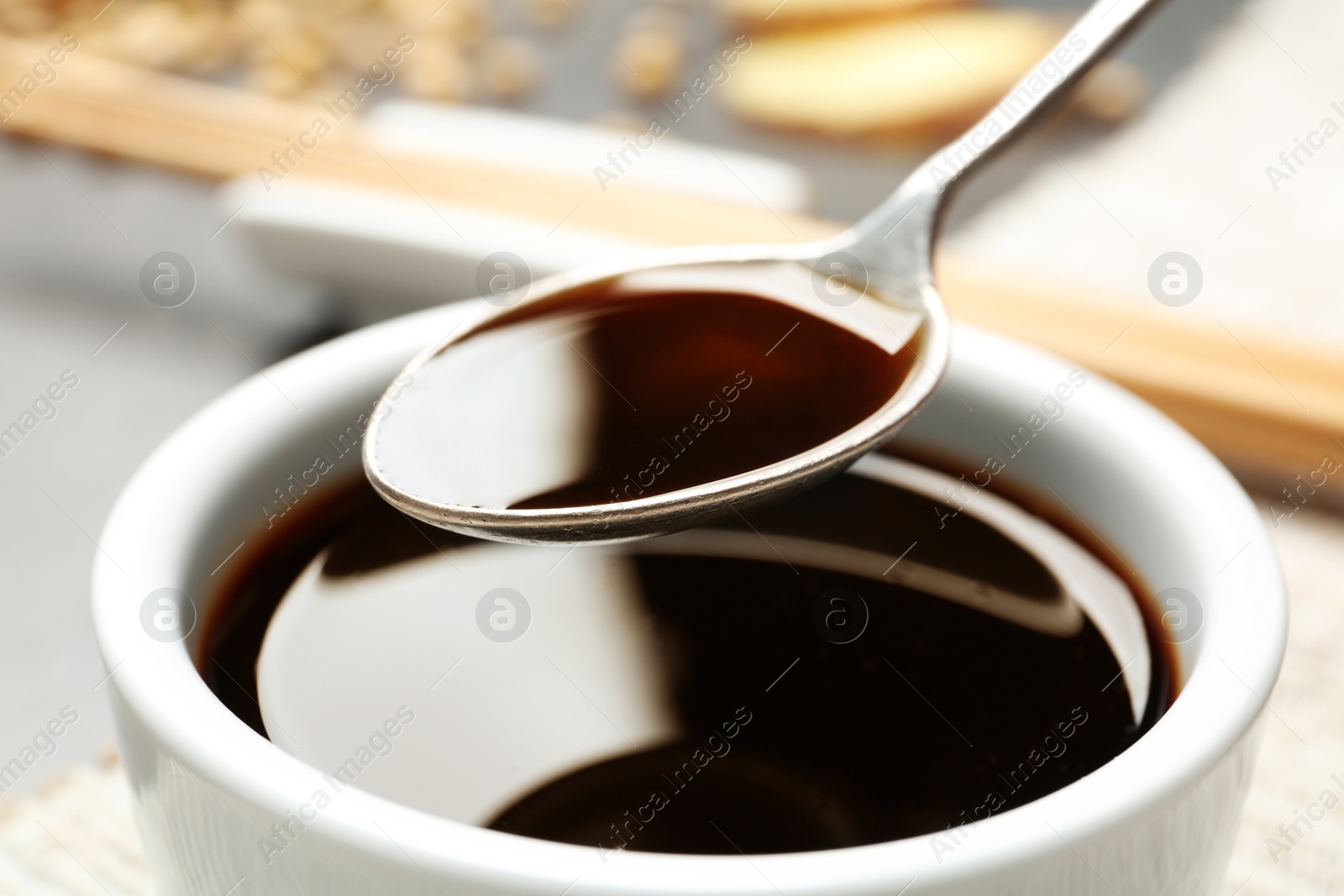 Photo of Spoon with soy sauce over bowl, closeup