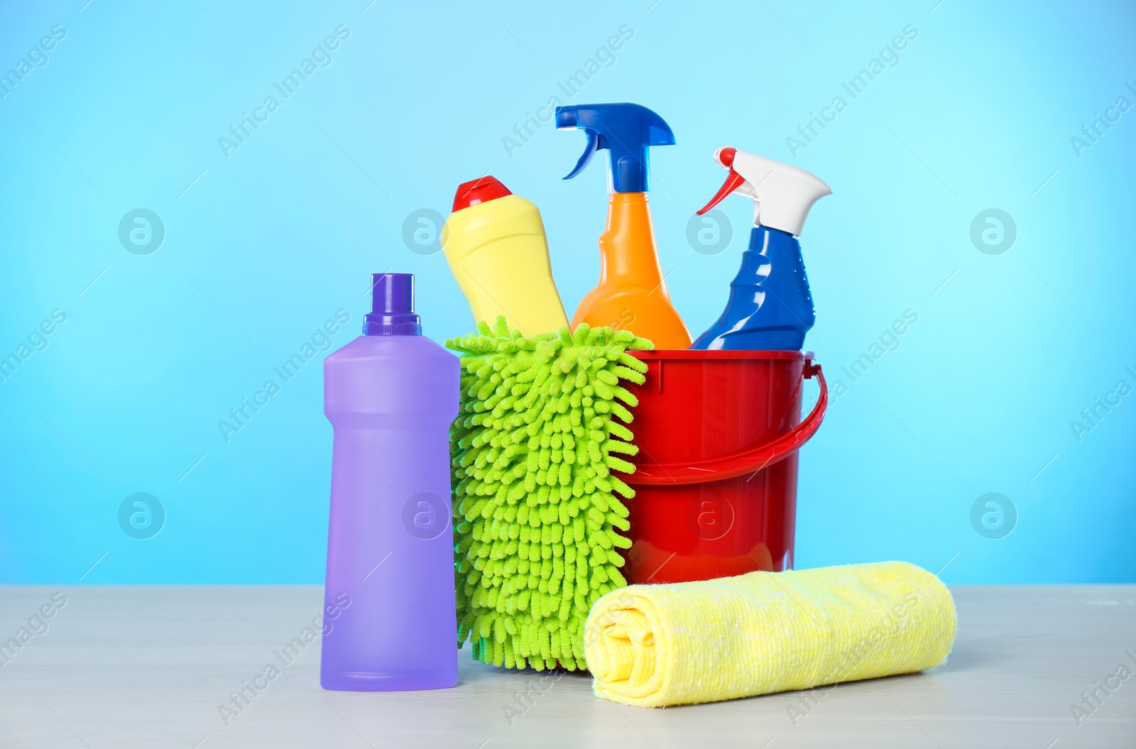 Photo of Bucket with different cleaning products and supplies on light table