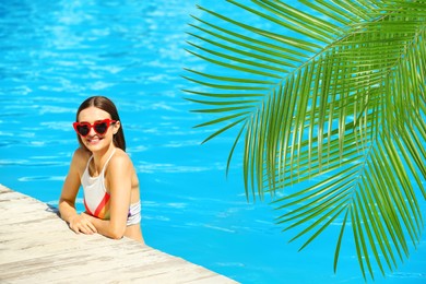 Image of View of beautiful green tropical leaves and young woman in swimming pool on sunny day