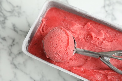 Photo of Container with delicious pink ice cream and scoop on marble table, top view