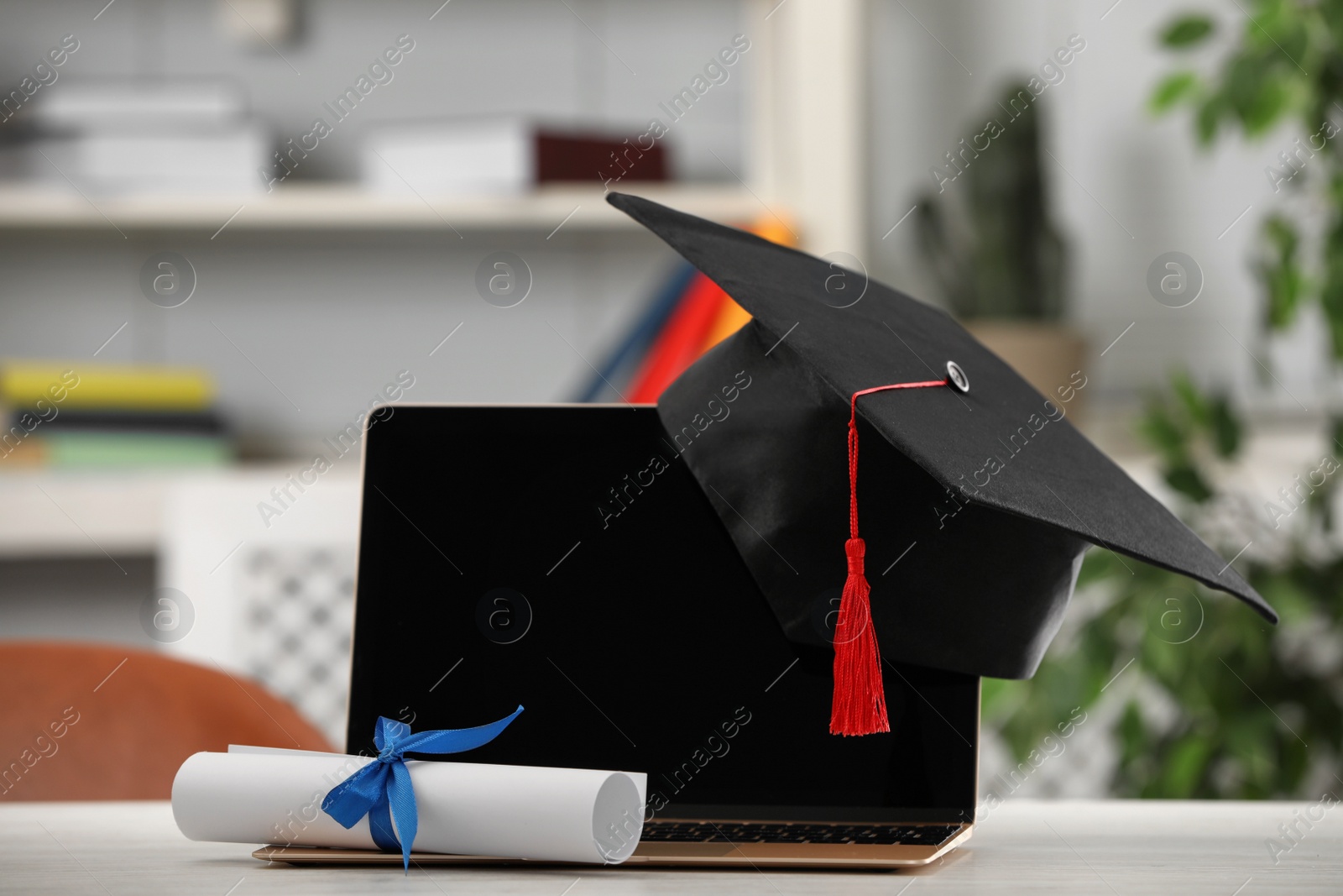 Photo of Graduation hat, student's diploma and laptop on white table indoors