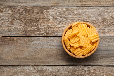 Photo of Bowl with delicious ridged potato chips on wooden table, top view. Space for text