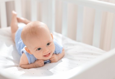 Cute little baby lying in crib at home, space for text