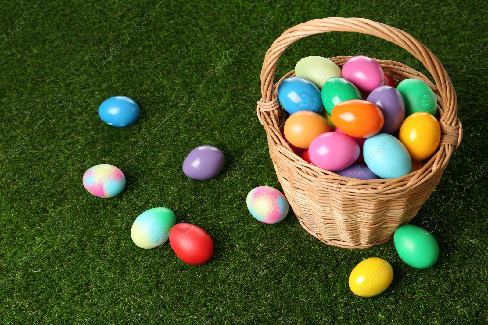 Photo of Wicker basket with bright painted Easter eggs on green grass