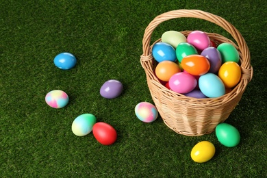 Photo of Wicker basket with bright painted Easter eggs on green grass