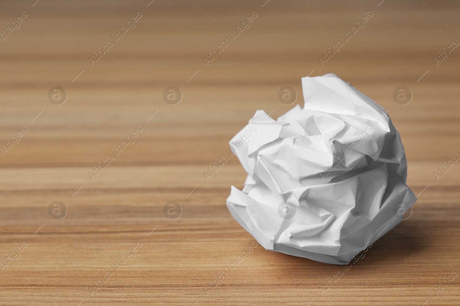 Photo of Ball of crumpled paper on wooden table, space for text