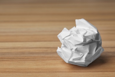 Photo of Ball of crumpled paper on wooden table, space for text