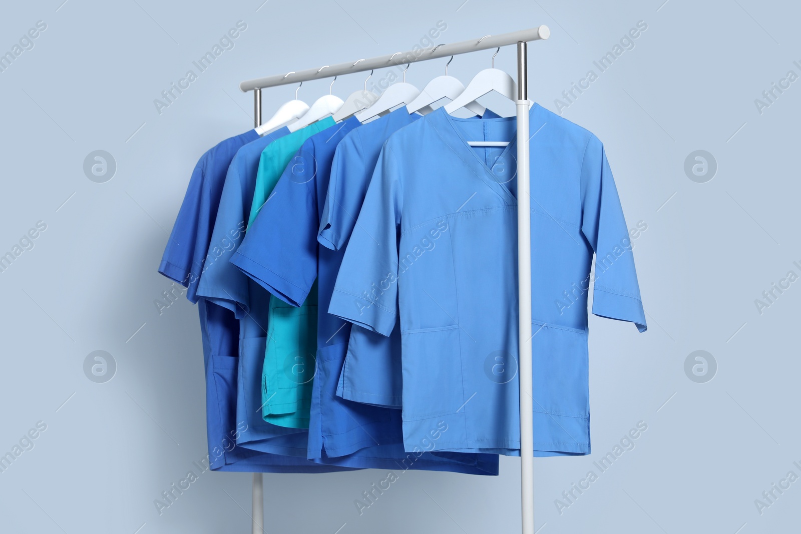 Photo of Different medical uniforms on rack against light grey background