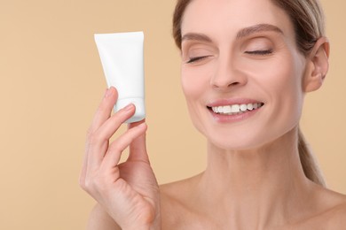 Woman holding tube of foundation on beige background