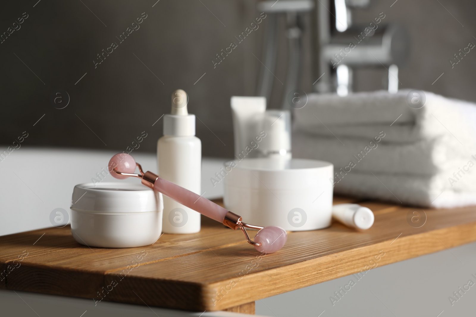 Photo of Bath tray with natural face roller and cosmetic products on tub