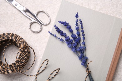 Photo of Preserved lavender flowers, scissors, twine and notebook on white textured table, flat lay