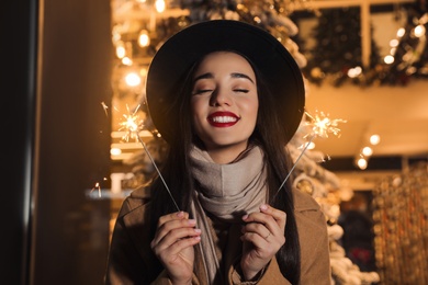 Photo of Woman in warm clothes holding burning sparklers on blurred background