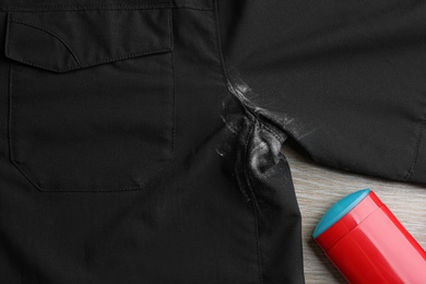 Black shirt with stain and deodorant on wooden background, closeup