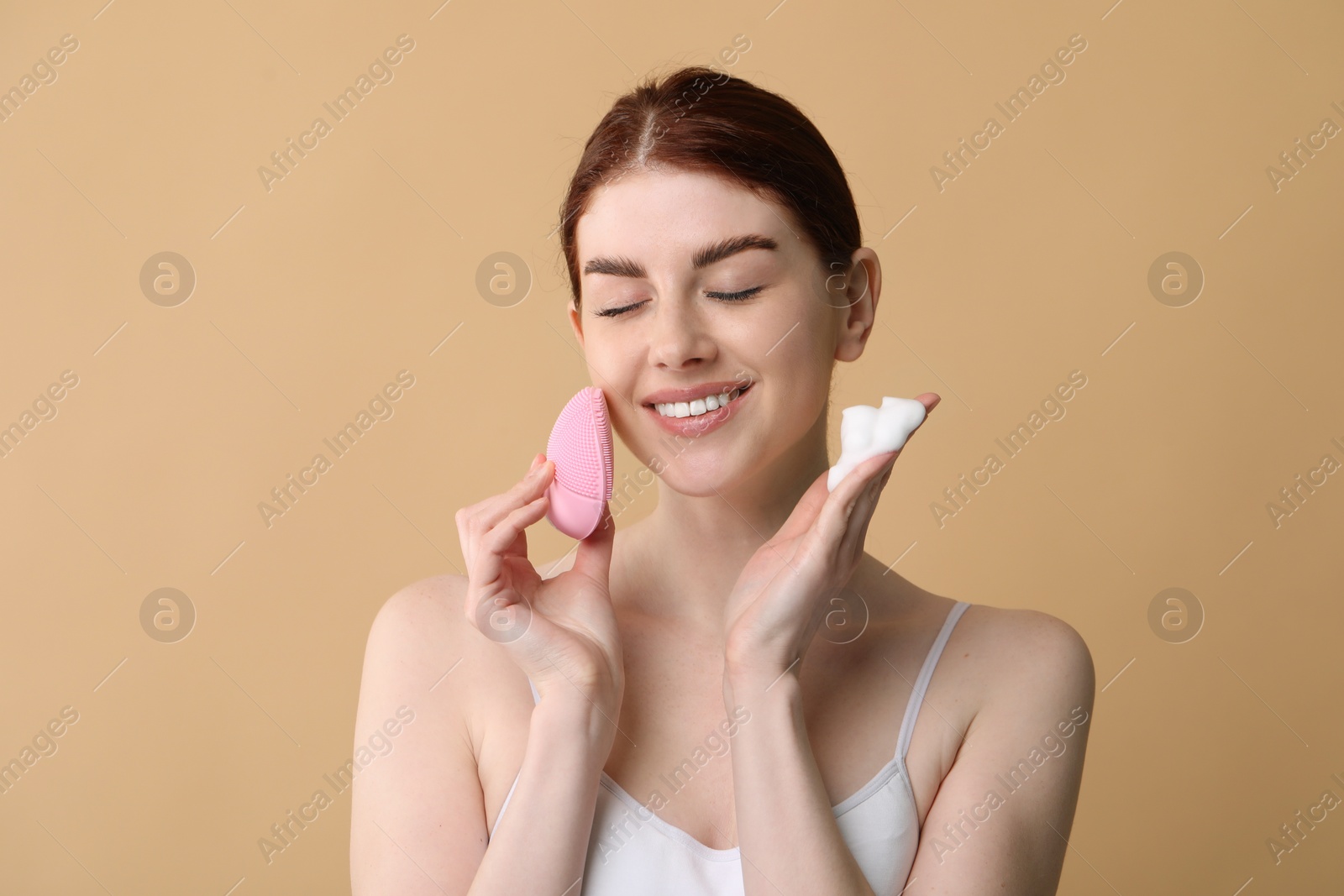 Photo of Washing face. Young woman with brush and cleansing foam on beige background