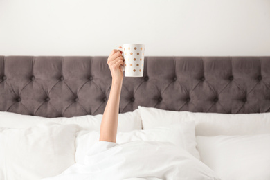 Woman with cup of coffee in bed, closeup. Lazy morning