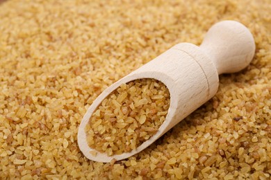 Photo of Wooden scoop on pile of uncooked bulgur, closeup view