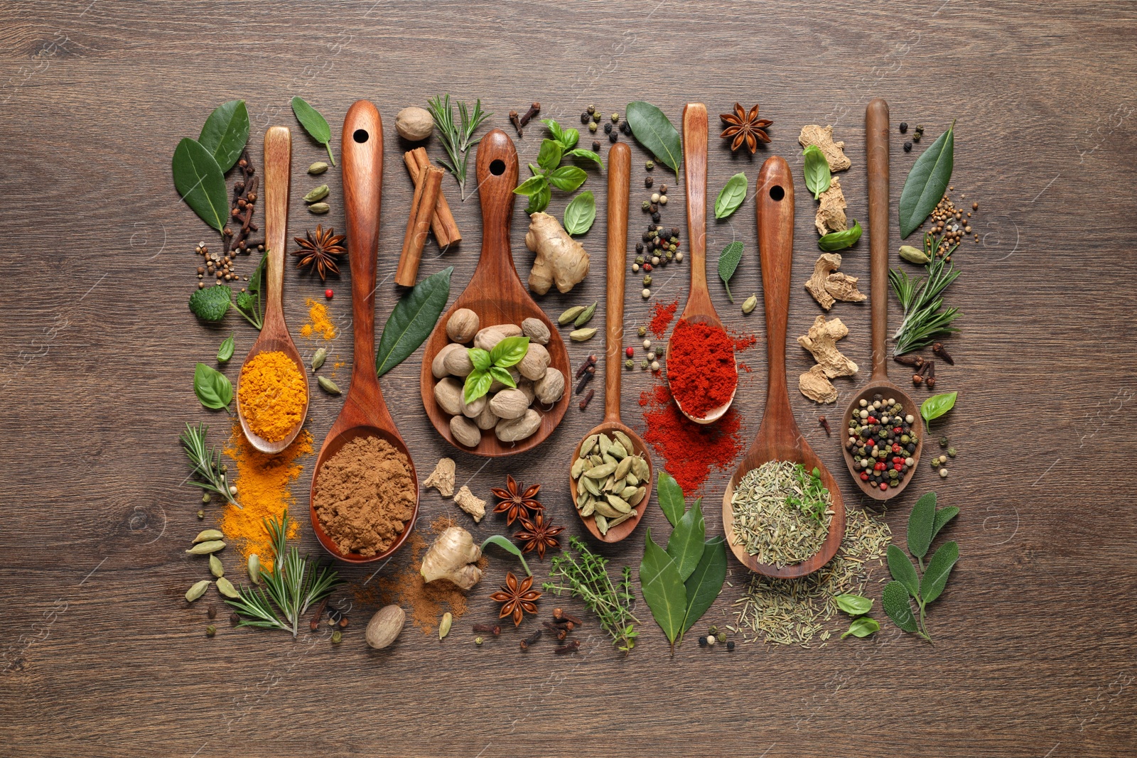 Photo of Different herbs and spices with spoons on wooden table, flat lay