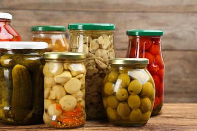 Photo of Jars of pickled vegetables on wooden table, closeup
