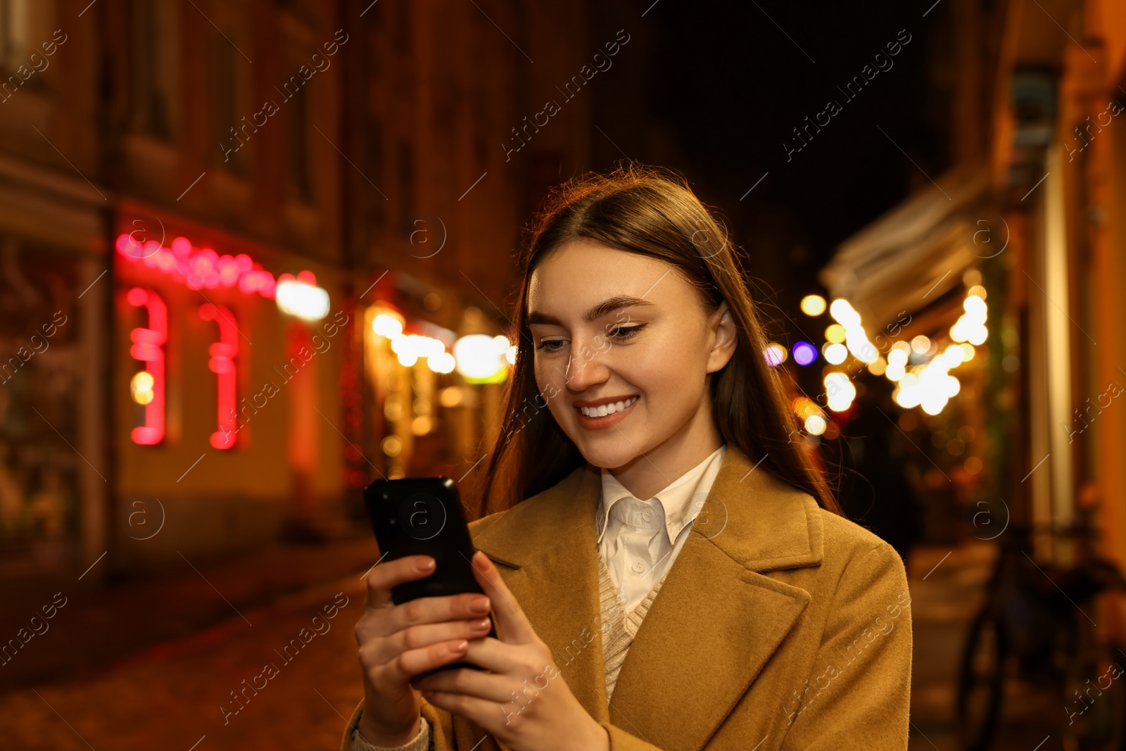 Photo of Smiling woman using smartphone on night city street. Space for text