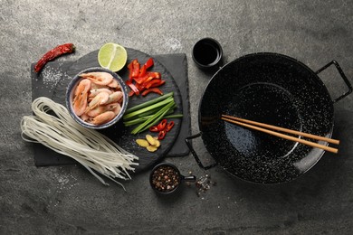 Flat lay composition with black wok, spices and products on dark textured table