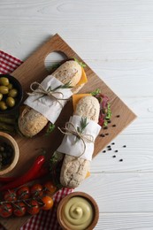 Photo of Delicious sandwiches with bresaola, cheese and other products on white wooden table, flat lay