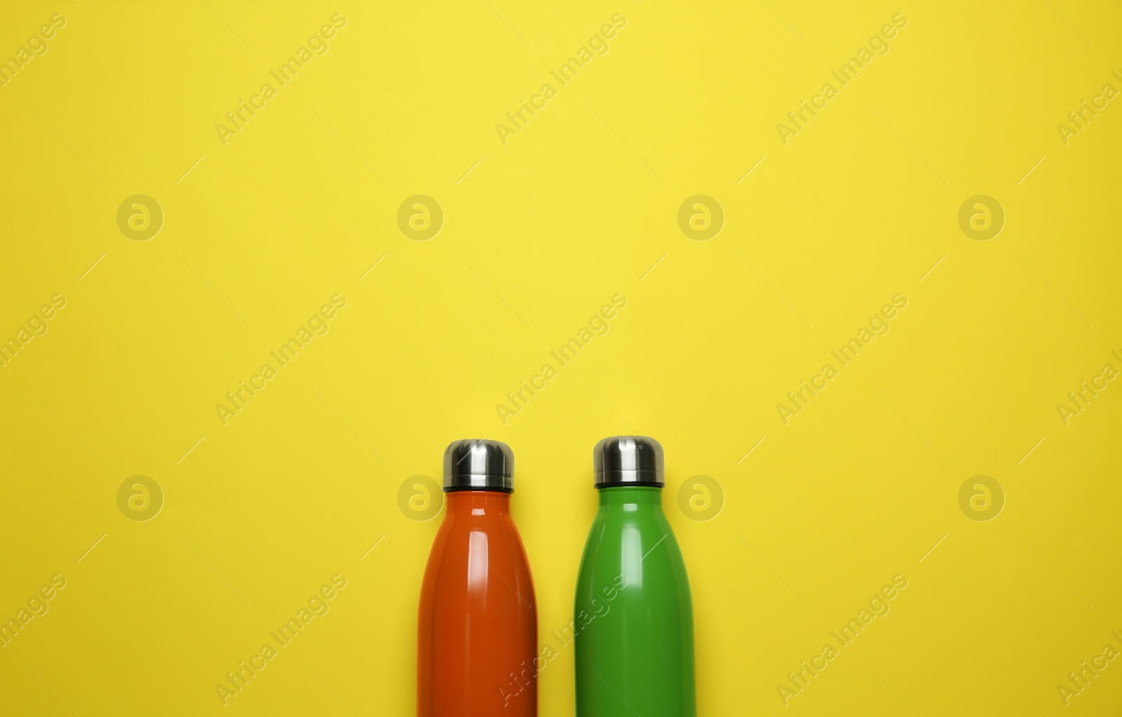 Photo of Modern thermo bottles on yellow background, flat lay. Space for text