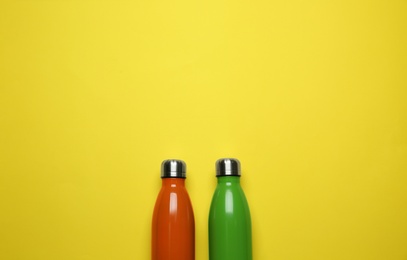 Photo of Modern thermo bottles on yellow background, flat lay. Space for text