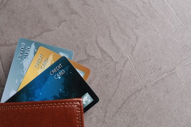 Credit cards and leather wallet on grey textured table, top view. Space for text