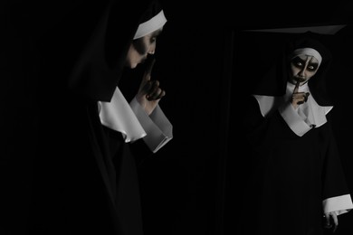 Scary devilish nun near mirror on black background. Halloween party look
