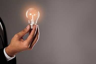 Photo of Businessman holding lamp bulb against gray background, closeup. Space for text