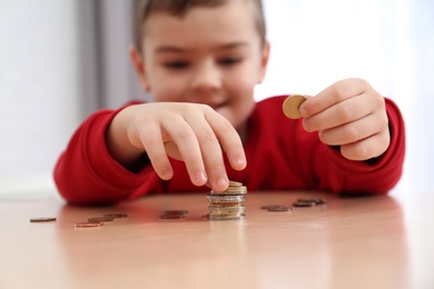 Cute little boy with coins at home, closeup. Counting money