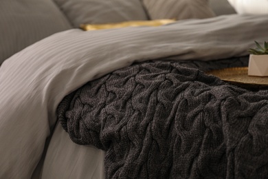 Photo of Knitted black plaid on bed indoors, closeup