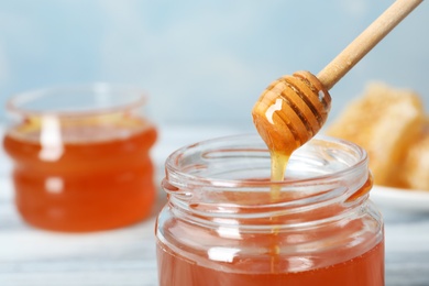 Photo of Sweet honey dripping from dipper into glass jar, closeup