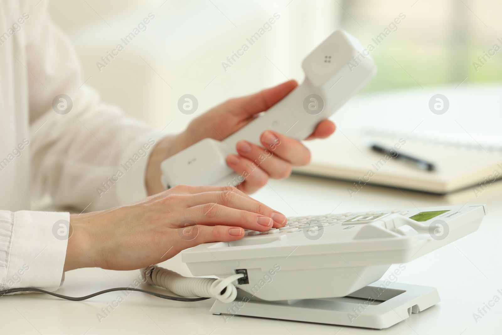 Photo of Assistant dialing number on telephone at white table, closeup