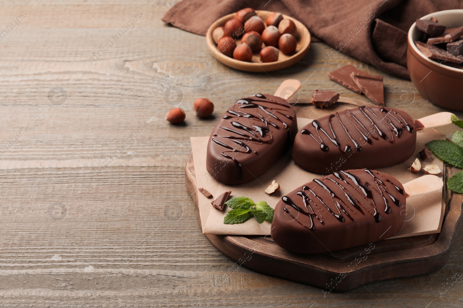 Photo of Delicious glazed ice cream bars, nuts and mint on wooden table. Space for text