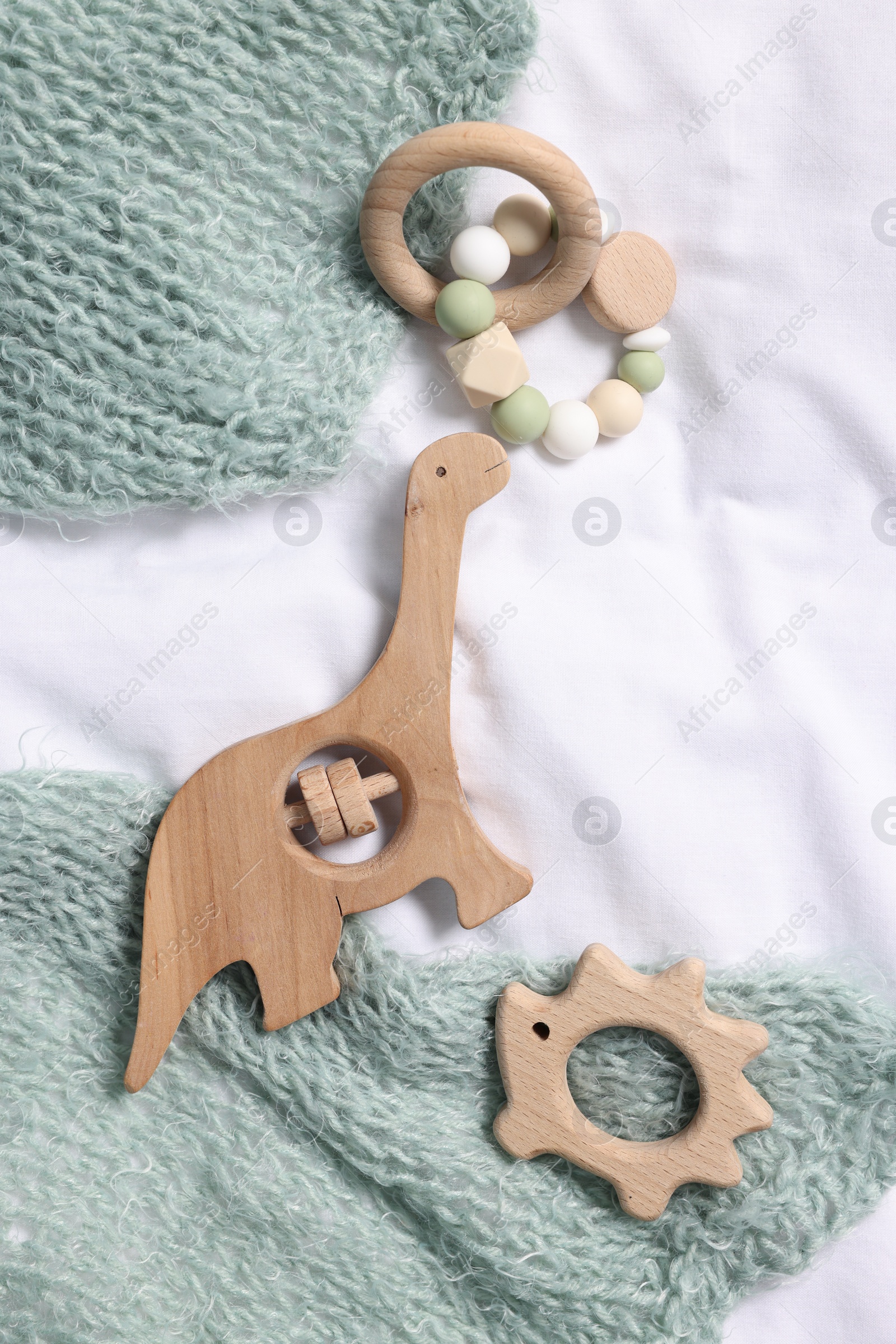 Photo of Baby accessories. Different rattles, teether and child's clothes on white fabric, flat lay