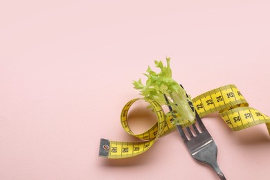 Photo of Fork with measuring tape and lettuce leaf on pale pink background, top view with space for text. Diet concept