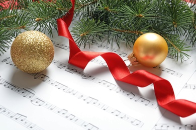 Fir tree branches with Christmas balls and ribbon on music sheets