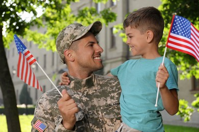 Photo of Soldier and his little son with American flags outdoors. Veterans Day in USA