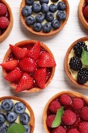 Photo of Tartlets with different fresh berries on white wooden table, flat lay. Delicious dessert