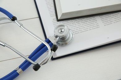 Photo of One new medical stethoscope and books on white wooden table, closeup