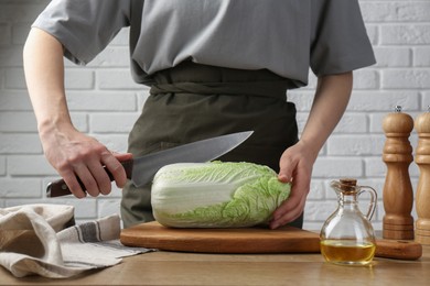 Woman cutting fresh Chinese cabbage at wooden table indoors, closeup