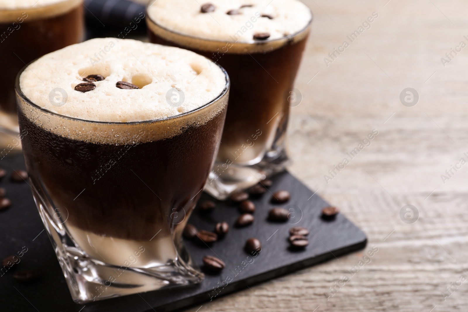 Photo of Glasses of tasty cocktail with coffee beans on wooden table, closeup