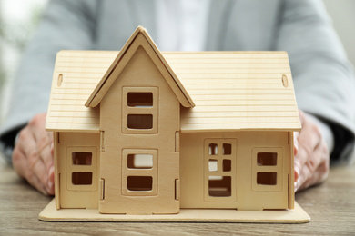 Photo of Real estate agent holding house model at wooden table, closeup