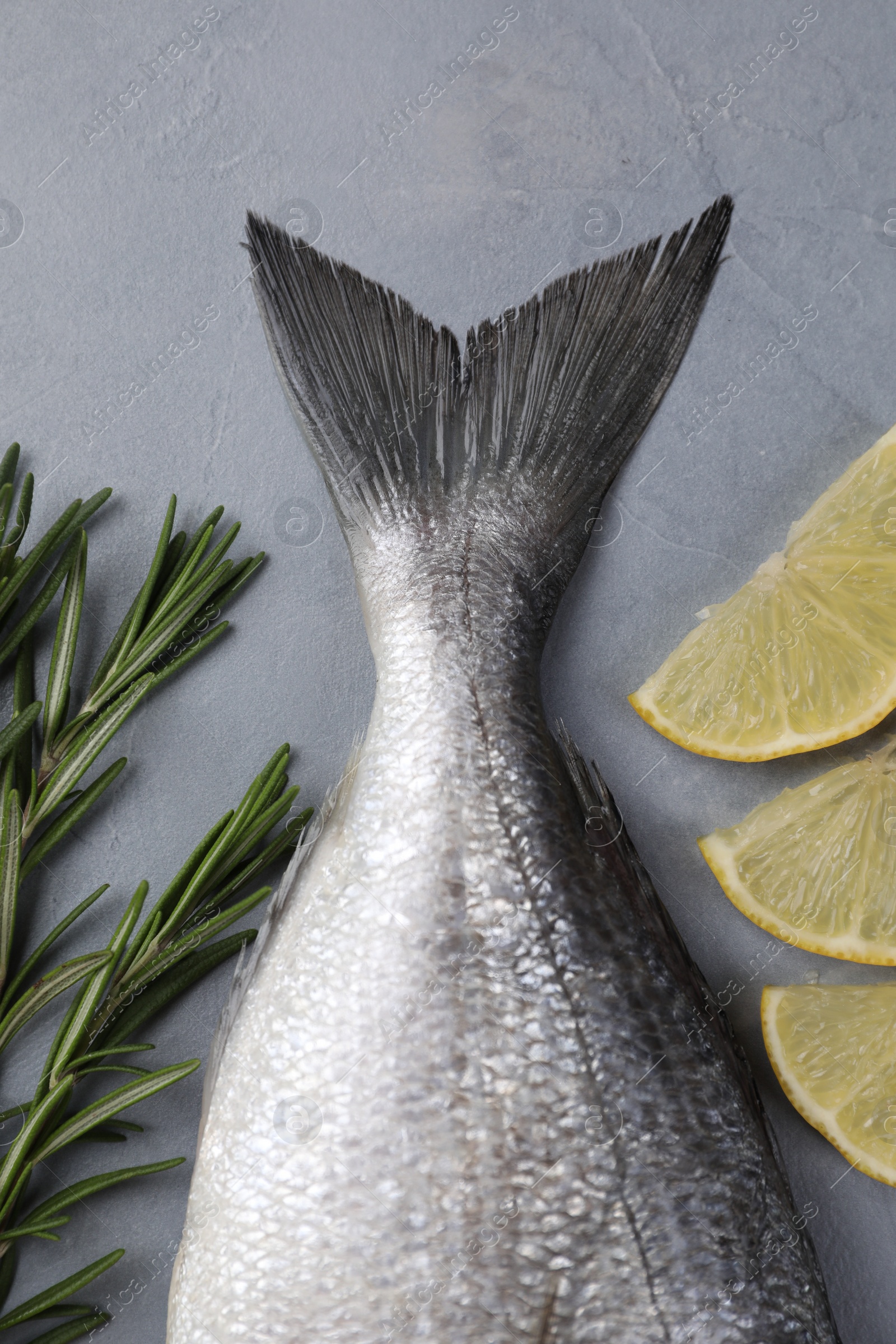 Photo of Fresh raw dorado fish, lemon slices and rosemary on grey table, flat lay