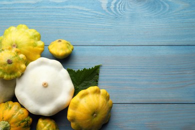 Fresh ripe pattypan squashes with leaf on light blue wooden table, flat lay. Space for text