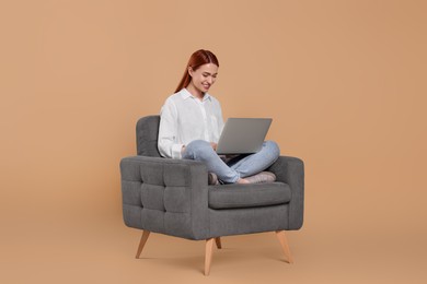 Photo of Smiling young woman working with laptop in armchair on beige background
